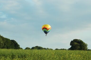 bunter Heißluftballon über einer Wiese vor blauem Himmel