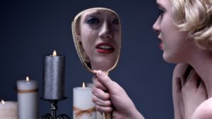 Blonde Frau mit Lippenstift schaut in Handspiegel, Träne auf Wange