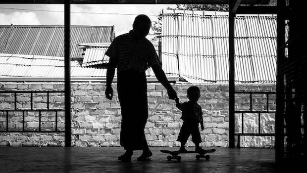 Erwachsener mit Kind auf Skateboard an der Hand, Schattenbild