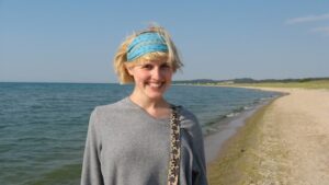 Frau mit blauem Haarband am Strand vor Wasser