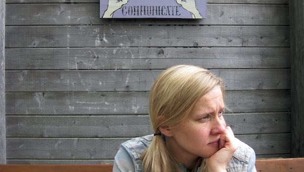 Nachdenkliche, blonde Frau und ein "Communicate-Schild" im Hintergrund