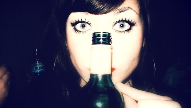 Frau mit großen Augen hinter Weinflasche