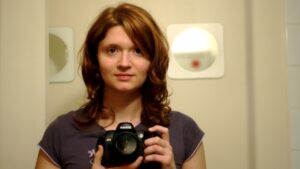 Frau mit roten Haaren und Kamera schaut in den Spiegel