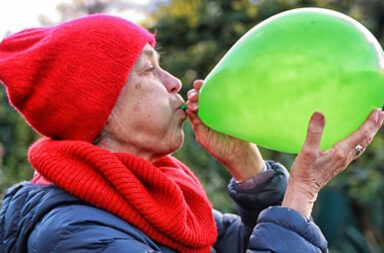 Ältere Frau mit roter Mütze pustet grünen Ballon auf