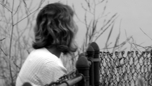 Frau in Rückansicht beim Gartenzaun