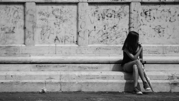 Frau sitzt allein vor einer Steinmauer.