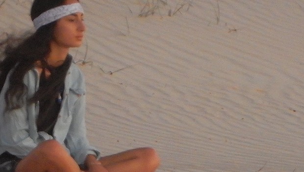 Frau mit Stirnband im Schneidersitz am Strand