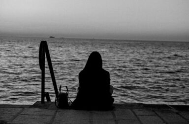 Frau sitzt auf Stufen und schaut aufs Wasser