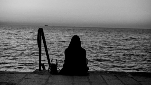 Frau sitzt auf Stufen und schaut aufs Wasser