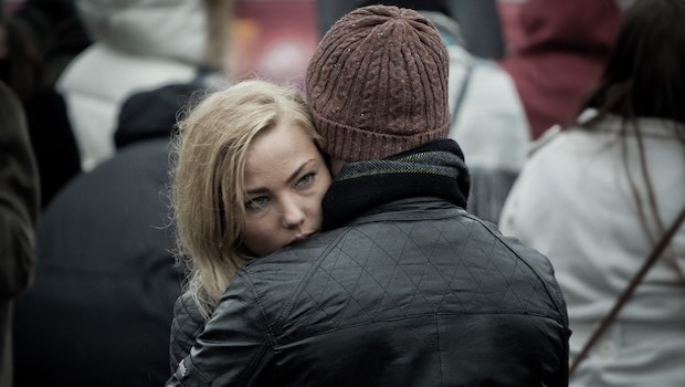 Frau umarmt Mann und schaut über seine Schulter.