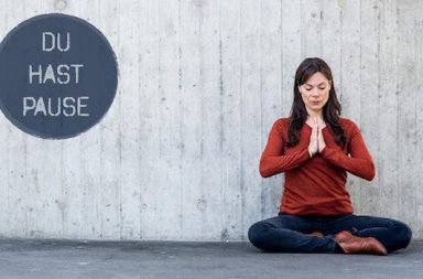 Frau in Yogapose, an der Wand die Aufschrift Du hast Pause