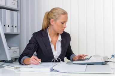 Geschäftsfrau im Büro sitzend am Taschenrechner