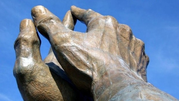 Steinskulptur zweier Hände vor blauem Himmel