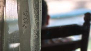 Hinterkopf im Stuhl hinter Gardine