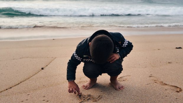 Junge malt in Sand am Strand mit Meer im Hintergrund