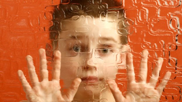 Kind mit Händen an der Glasscheibe, im Hintergrund orange Wand