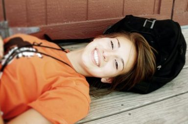 Mädchen mit orangem Shirt liegt auf Dielenboden und lacht