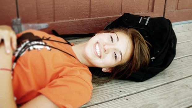 Mädchen mit orangem Shirt liegt auf Dielenboden und lacht