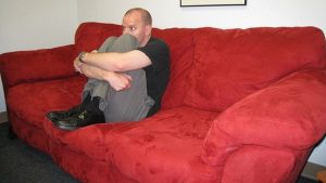 Mann sitzt auf rotem Sofa