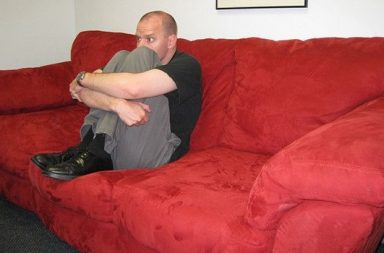 Mann sitzt auf rotem Sofa