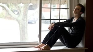 Mann sitzt auf Fensterbank mit nackten Füßen