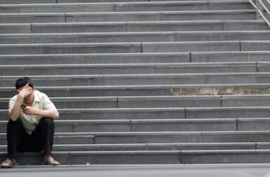 Mann mit Hand an der Stirn sitzt auf Treppe