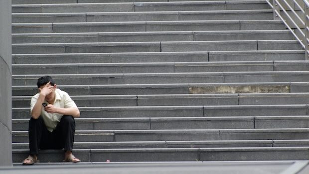 Mann mit Hand an der Stirn sitzt auf Treppe