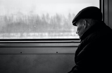 Mann mit Mütze sitzt im Zug und schaut nachdenklich aus dem Fenster