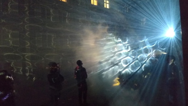 Zwei Menschen stehen nachts vor Mauer und betrachten Lichtquelle