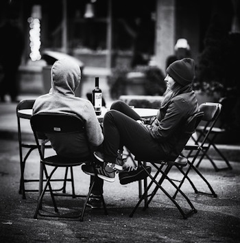 Zwei Menschen sitzen draußen, an Tisch mit Weinflasche