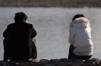 Paar sitzt am Wasser mit Abstand voneinander