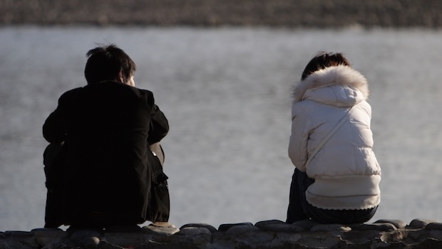 Paar sitzt am Wasser mit Abstand voneinander