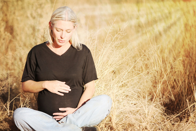 Schwangere Frau sitzt im Feld