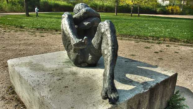 Skulptur Park liegend Arme schuetzend Gesicht