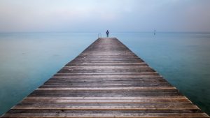 Mensch mit Rucksack auf langem Steg am Meer